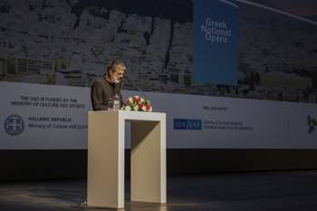 A man gives a speech on stage with a backdrop of a screen that writes